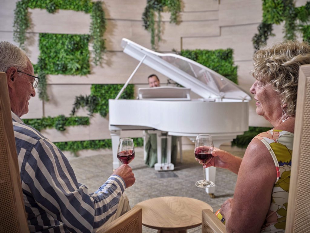 2 people drinking red wine and watching a pianist play in the Wellness Centre