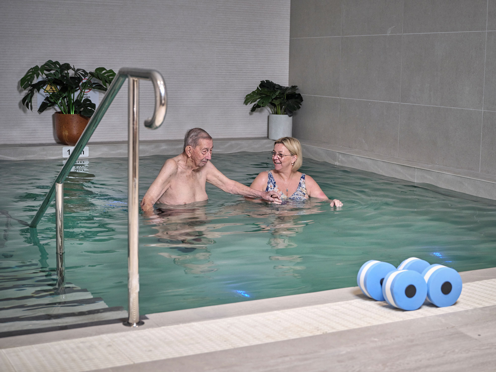 A man and carer go swimming in the hydrotherapy pool in the Greenwich Place Wellness Centre