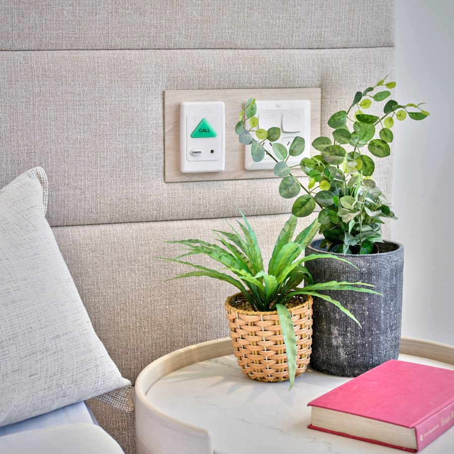 Greenwich Place Deluxe bedside table with book, plants and emergency call button
